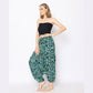 A woman stands against a white background wearing a strapless tube top and loose, patterned teal harem pants. She pairs this chic ensemble with sandals, and her hair is styled in loose waves as she gazes to the side.