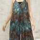 A person wearing a flowy, sleeveless dress with intricate geometric patterns in teal, brown, and black. The background is a textured, light-colored wall.