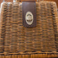 A close-up of a brown woven handbag with a leather strap and a metallic twist lock. The texture of the weave is detailed, showcasing the craftsmanship. The lock is centered on the strap.