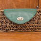 A clutch purse made of woven rattan with a green leather flap and silver clasp, placed against a wood background. A clutch purse made of woven rattan with a green leather flap and silver clasp, placed against a wood background.