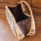A rattan purse with a curved handle and a brown fabric interior sits on a wooden surface. The handbag is open, revealing its spacious interior.