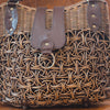 A large rattan bag with intricate patterns and leather accents. The front features a leather flap with a metal ring detail, blending rustic texture with modern elements for a striking look.