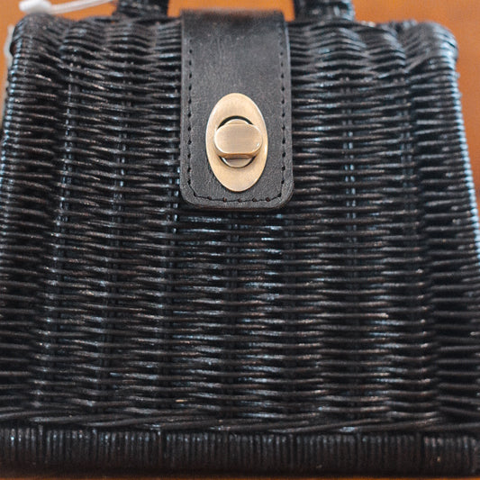 A sleek black woven rattan purse with a leather strap and a brass twist-lock clasp on the front. The texture of the weave is beautifully visible, and the clasp is perfectly centered on the bag.