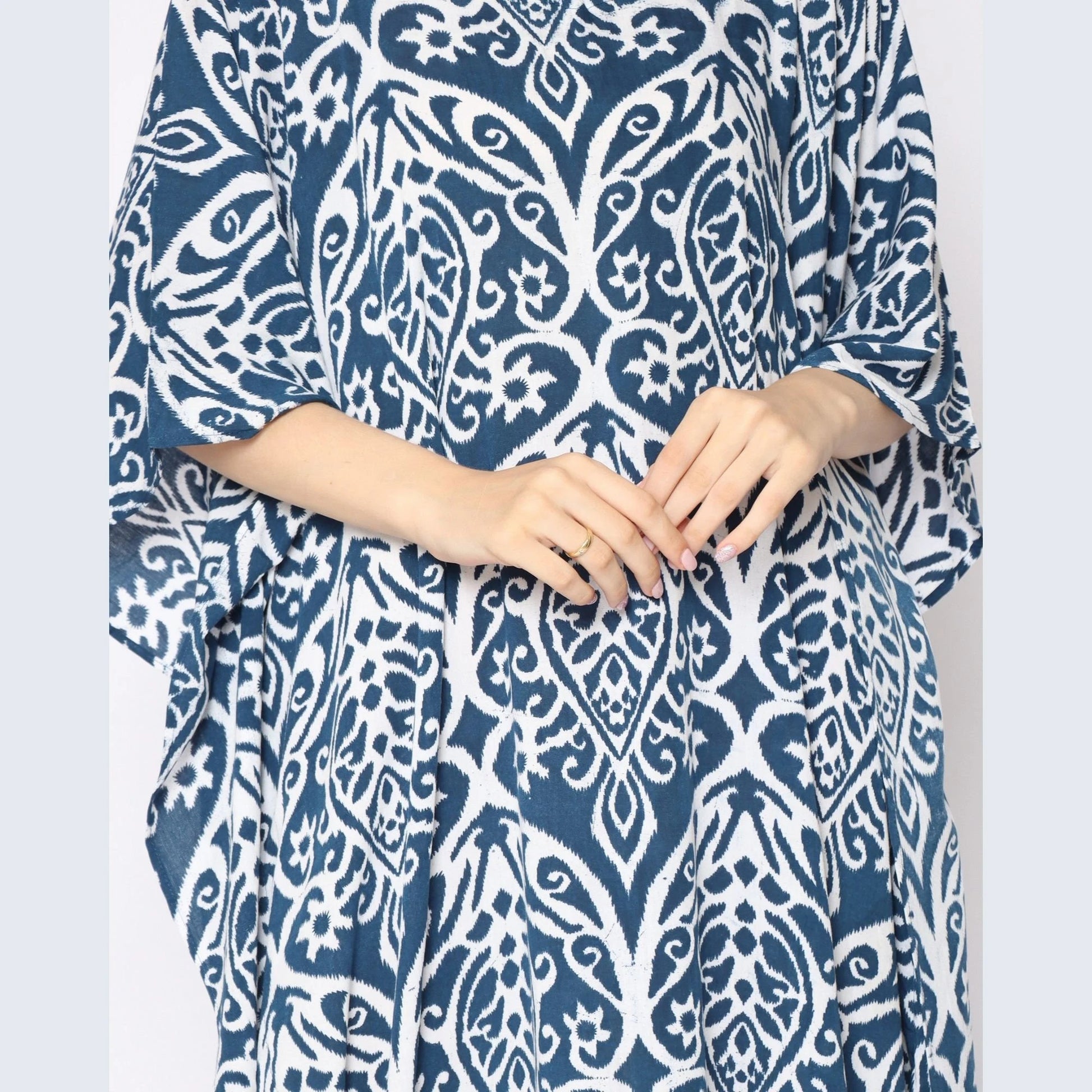 A person wearing a stylish blue and white patterned caftan with their hands gently clasped in front. The detailed design features intricate floral and geometric shapes, creating an elegant and timeless look.
