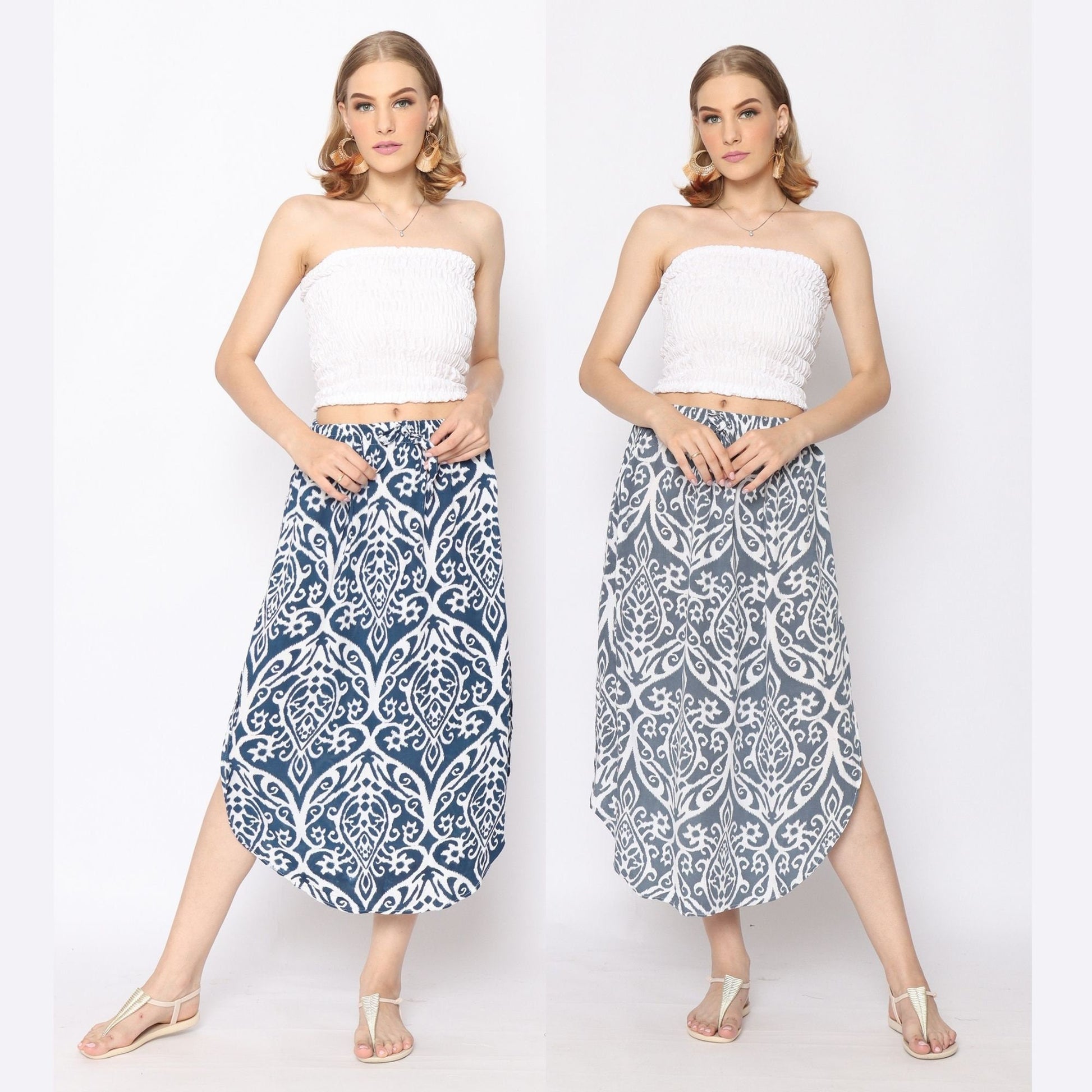 Two images showcase the same woman in a white strapless top paired with skirts featuring side slits: one blue and white, the other gray and white. Her short hair complements her neutral makeup as she poses in sandals, hands casually resting in her skirt pockets.