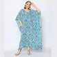 A woman in a flowing blue caftan with an intricate white pattern poses confidently. She stands against a plain background, wearing silver sandals and hoop earrings, her hair styled in waves.
