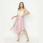 A woman strikes a pose against a plain background, wearing a white crochet halter top paired with vibrant pink panel pants featuring a diamond hem. Her light brown hair complements the ensemble, and strappy sandals complete her chic look.