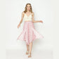A woman strikes a pose against a plain background, wearing a white crochet halter top paired with vibrant pink panel pants featuring a diamond hem. Her light brown hair complements the ensemble, and strappy sandals complete her chic look.