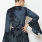 A person with hair in a bun is wearing a dark blue and black boho top featuring flared sleeves and a matching skirt. The person is facing away, standing against a plain white background.
